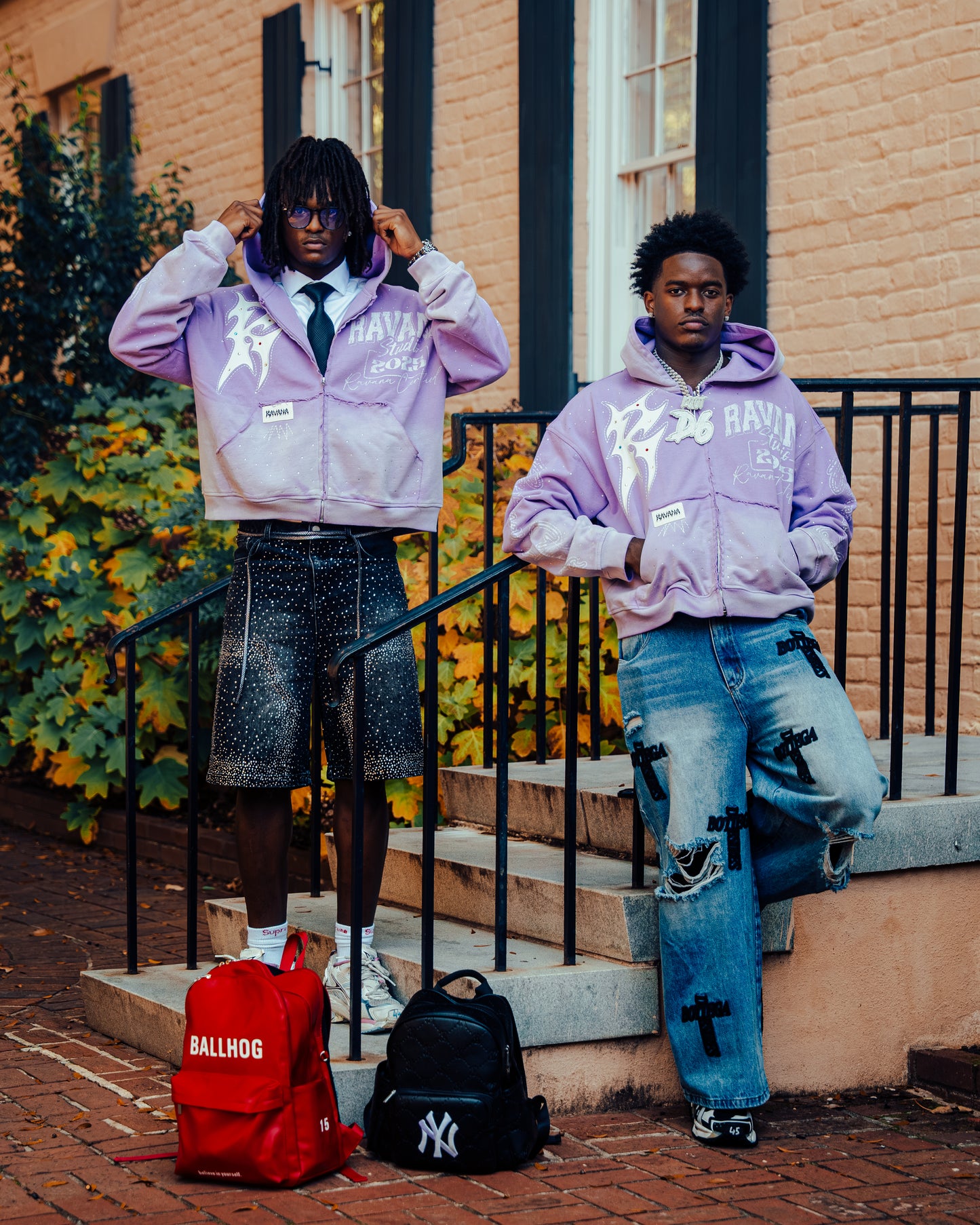 Two individuals wearing matching purple hoodies with visible branding, standing on steps outdoors.